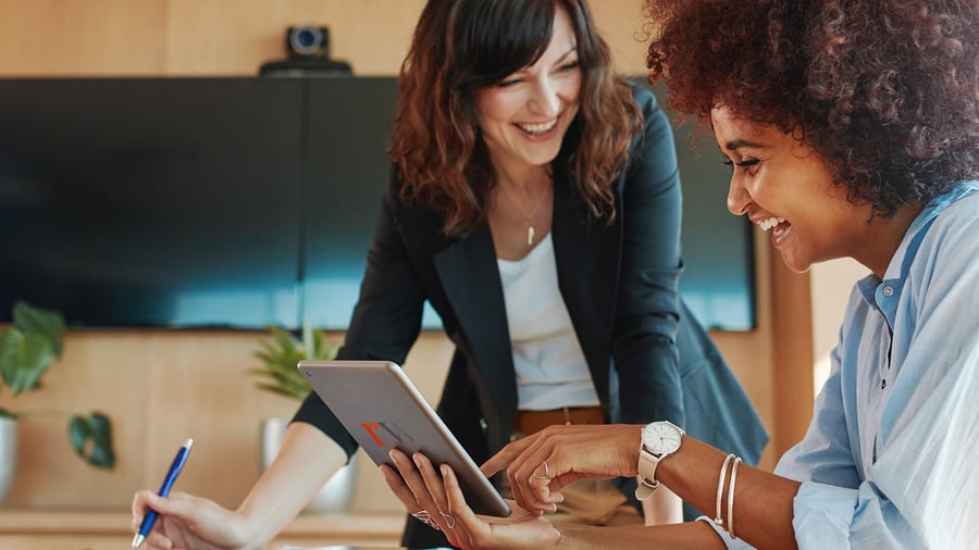 Diverse corporate, female exes looking at a tablet that has the ReadyWorks logo and looking pleased with the results on screen.