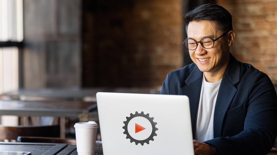Asian-american business man, sitting in a cafe, working remotely on their laptop that has a ReadyWorks logo 