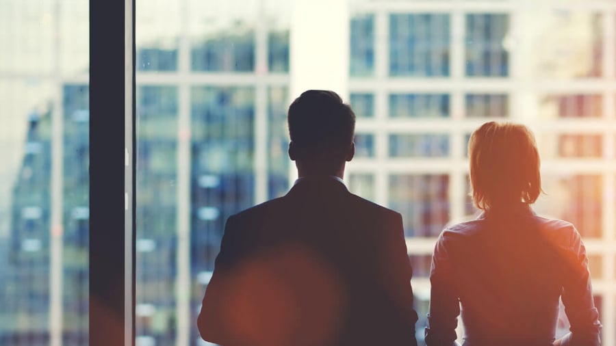 silhouettes of professional looking man and woman looking out into a city-scape from a high rise office